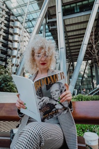 a woman reading a magazine on a bench in front of a building