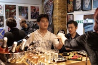 a group of people standing at a bar with bottles of wine